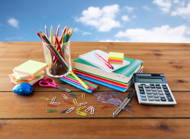 educación, útiles escolares, arte, creatividad y concepto de objeto: cierre de papelería en una mesa de madera sobre el cielo azul y el fondo de las nubes