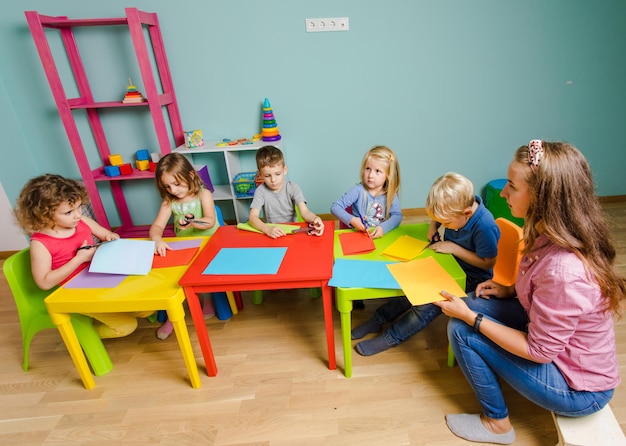 Educador y lindos niños en edad preescolar están haciendo coloridas postales.