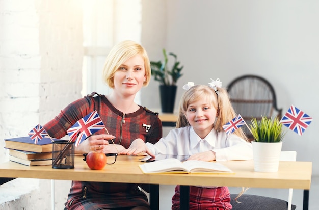 Educadora de inglés y niña inteligente mesa de trabajo sonriente con libros bandera británica y concepto de idioma educativo para niños de apple