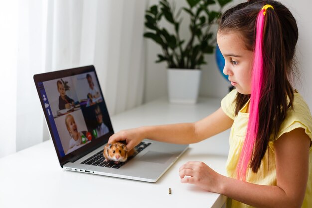 Educar en casa. La muchacha del niño hace la tarea con el hámster del animal doméstico. Hámster de jengibre divertido sentado en la mesa donde el niño está escribiendo. De vuelta a la escuela.