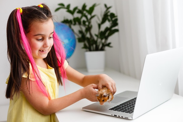 Educar en casa. La muchacha del niño hace la tarea con el hámster del animal doméstico. Hámster de jengibre divertido sentado en la mesa donde el niño está escribiendo. De vuelta a la escuela.