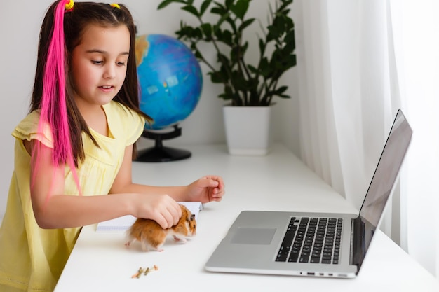 Eduque em casa. menina criança fazer lição de casa com hamster de estimação. engraçado hamster ruivo sentado na mesa onde a criança está escrevendo. de volta à escola.