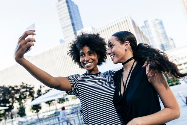 Ee.Uu., la ciudad de Nueva York, dos mujeres jóvenes felices teniendo selfie con smartphone