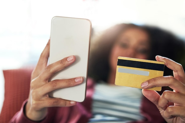 Sin efectivo, no hay problema Foto de una mujer joven que usa un teléfono móvil y una tarjeta de crédito en el sofá de casa