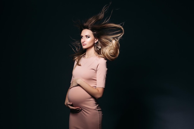 Efecto ventoso en el retrato de estudio de una hermosa mujer embarazada con vestido rosa abrazando el vientre Mujer elegante y con estilo posando mirando al costado Concepto de moda y apariencia de embarazo