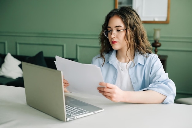 Effiziente Geschäftsfrau, die Finanzdaten mit einem Laptop und Buchhaltungsunterlagen verwaltet