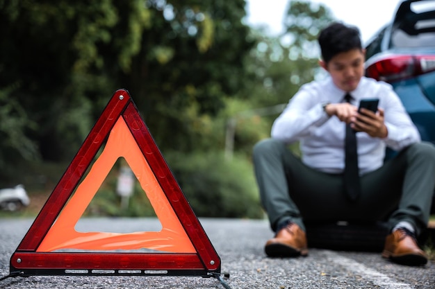 Foto eficiencia y confianza en exhibición como un joven empresario cambia la rueda de un coche roto mientras un hombre maduro preocupado mira un cartel de triángulo rojo advierte a los conductores del obstáculo por delante