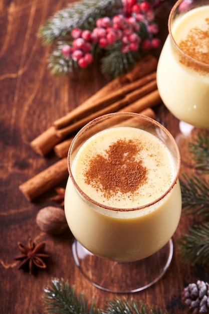 Eggnog Christmas. Leite, rum e canela de coquetel de inverno delicioso servidos em dois copos com biscoitos de açúcar em forma de estrela de shortbread, ramo de abeto sobre a mesa de prancha de madeira branca. Fechar-se. Brincar.