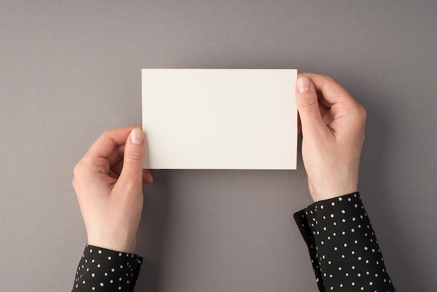 Egoperspektive Foto von Frauenhänden, die eine weiße Papierkarte auf isoliertem grauem Hintergrund mit Copyspace halten