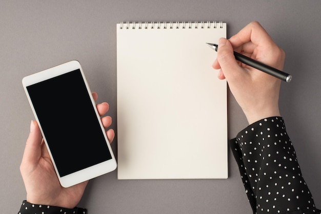 Egoperspektive Foto von Frauenhänden mit Stift und offenem Planer des Smartphones auf isoliertem grauem Hintergrund mit Leerzeichen