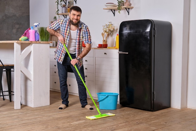 Ehemann Haushälterin reinigt die Küche junger glücklicher Mann mit grünem Mopp wäscht den Boden