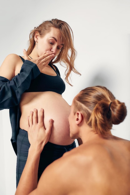 Ehemann küsst den Bauch seiner schwangeren Frau isoliert auf weißem Hintergrund