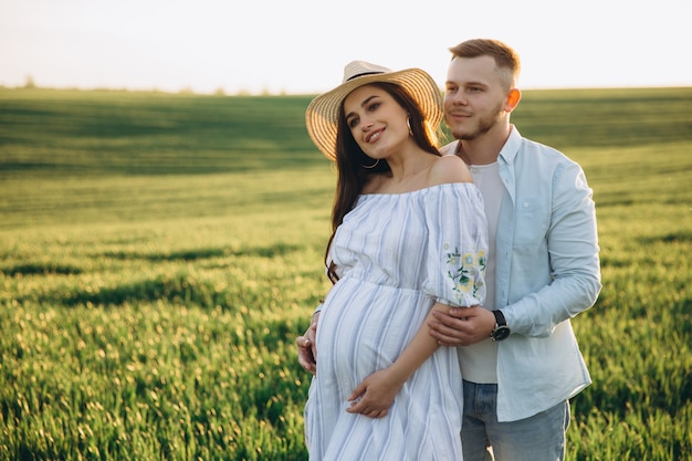 Ehemann und seine schwangere Frau gehen bei Sonnenuntergang auf dem Feld draußen spazieren. Thema romantische Schwangerschaft im Freien.