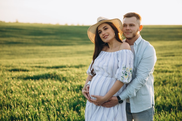 Ehemann und seine schwangere Frau gehen bei Sonnenuntergang auf dem Feld draußen spazieren. Thema romantische Schwangerschaft im Freien.