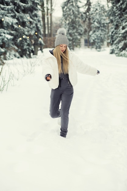 Ehrfürchtige blonde Frau, die mit Schnee im Wald spielt