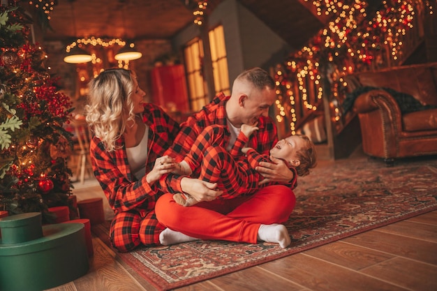 Ehrliche, authentische, süße, glückliche Familie in rot karierten Pyjamas verbringt Zeit zusammen in der weihnachtlich dekorierten Lodge