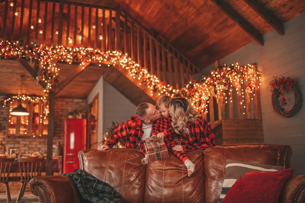 Ehrliche, authentische, süße, glückliche Familie in rot karierten Pyjamas verbringt Zeit zusammen in der weihnachtlich dekorierten Lodge