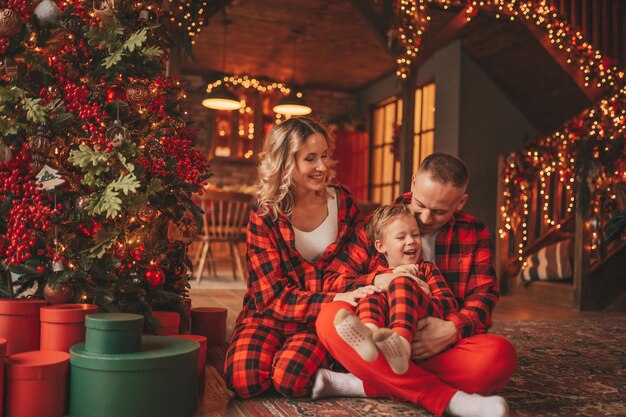 Ehrliche, authentische, süße, glückliche Familie in rot karierten Pyjamas verbringt Zeit zusammen in der weihnachtlich dekorierten Lodge