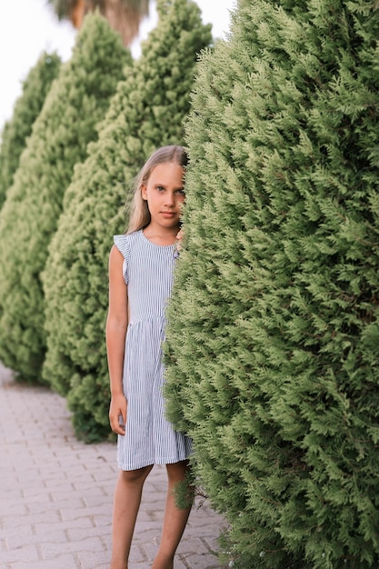 Ehrliches kaukasisches glückliches kleines Mädchen von acht Jahren mit langen blonden Haaren und grünen Augen auf dem Hintergrund grüner Pflanzen während eines Sommerurlaubs reisen gen z psychisches Gesundheitskonzept