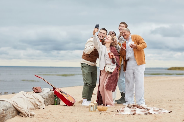 Foto ehrliches porträt in voller länge von verschiedenen gruppen von freunden, die im herbst ein selfie-foto am strand machen, platz kopieren