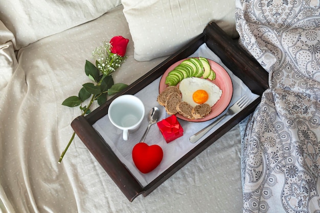 Ei, Avocado, Brot, Kaffee, Geschenk und Rose auf einem hölzernen Tablett Intime Atmosphäre für den Valentinstag