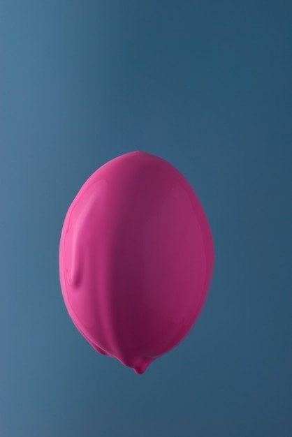 Ei in rosa Farbe fließt nach unten. Auf blauem Hintergrund. Minimalistische Osterkarte.