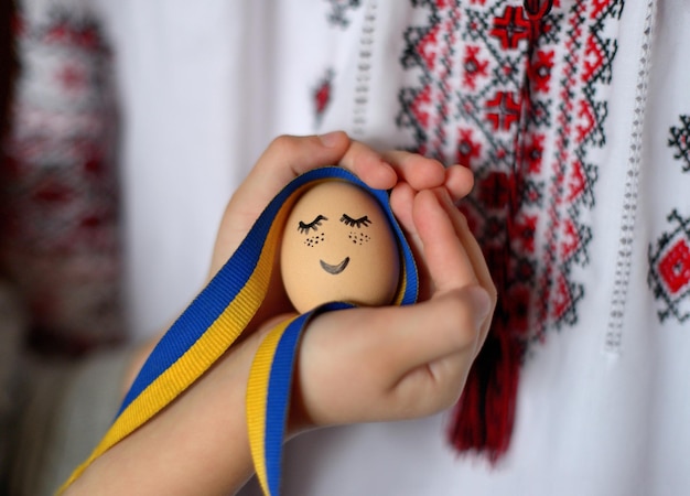 Ei mit bemaltem Gesicht und ukrainischem Band und ukrainischem Ornament auf unscharfem Hintergrund