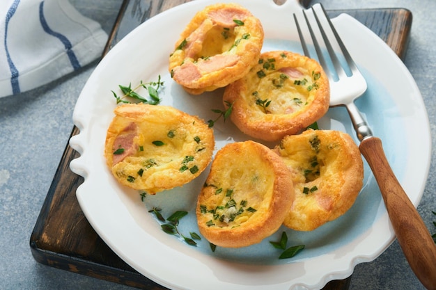 Ei-Muffins mit Frühlingszwiebeln, Speck, Käse und Tomaten auf weißem Teller auf hellem Hintergrund Gesundes proteinreiches und kohlenhydratarmes Frühstück zum Verzehr bereit