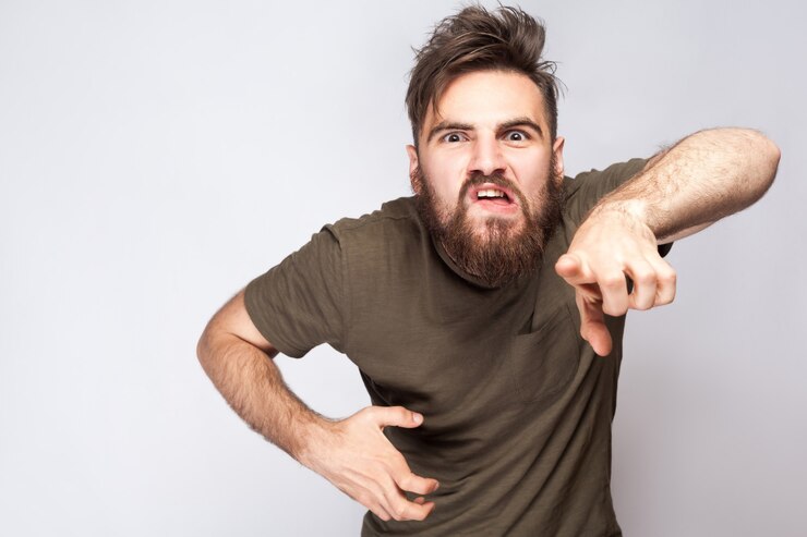 Foto ei você! retrato de homem barbudo com raiva louco com camiseta verde escuro contra um fundo cinza claro. tiro do estúdio. .