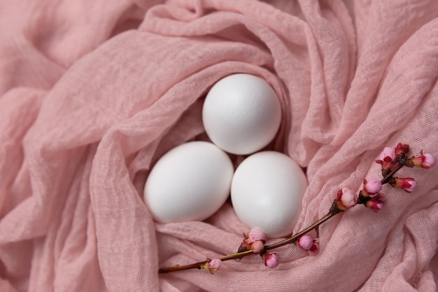 Eier auf einem rosa Stoff mit dem Dekor eines blühenden Aprikosenzweigs