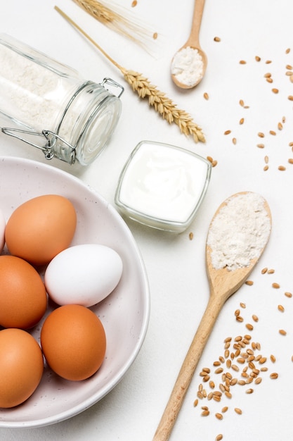 Eier in weißer Schüssel Mehl in Holzlöffel und im Glas Weizenkörner und Quelle der weißen Weizenoberfläche Draufsicht