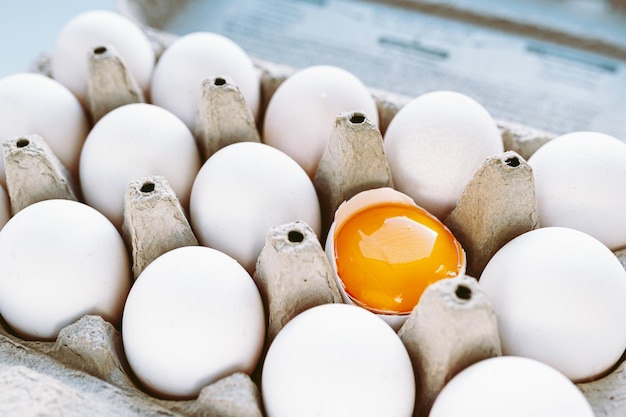 Eier mit weißer Schale und ein zerbrochenes Ei mit Eigelb in Recycling-Kartonschale. Konzept der Vielfalt,