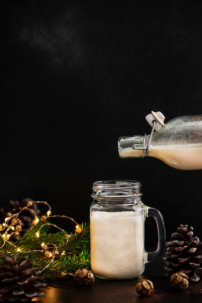 Eierlikör traditionelles alkoholisches Weihnachtsgetränk mit Zimt und Muskatnuss. Eierlikör gießt aus einer Flasche in ein Glas. Winterferien Stimmung. Dunkler Hintergrund