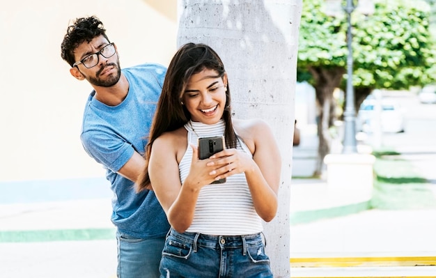 Eifersüchtiger Freund, der das Handy seiner Freundin im Park ausspioniert. Eifersüchtiger Mann, der seine Freundin ausspioniert, die auf dem Handy SMS schreibt