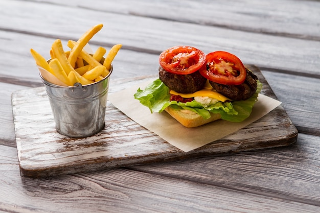 Eimer gefüllt mit Pommes. Tomatenscheibe und gegrilltes Fleisch. Zutaten für leckeren Hamburger. Das sollte dir schmecken.