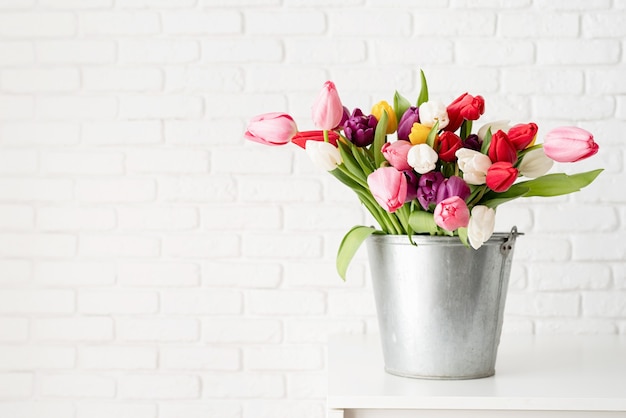 Eimer mit frischen Tulpenblumen über weißem Backsteinmauerhintergrund