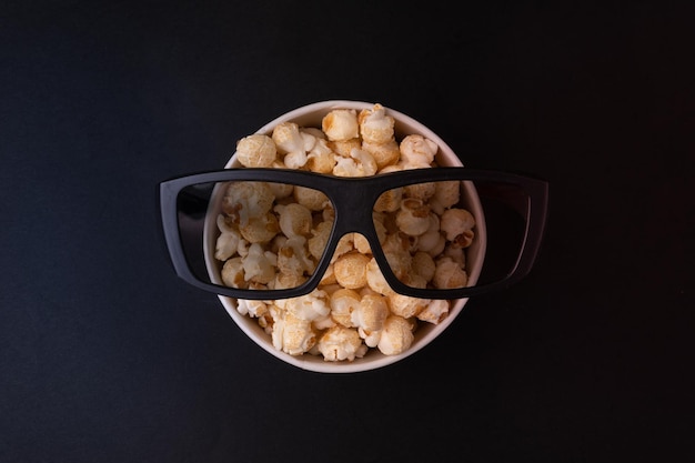 Eimer mit Karamell-Popcorn und Brille für 3D-Filme auf schwarzem Hintergrund Draufsicht Das Konzept eines Banners oder Werbung für ein Kino Platz für Text