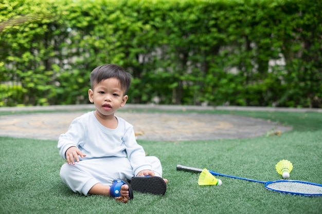 Ein 1-jähriger asiatischer Junge in blauer Kleidung sitzt zu Hause beim Badminton