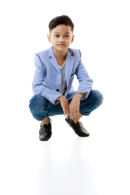 Ein 10-jähriger asiatischer Junge in einer Freizeitjacke sitzt schlau und glücklich und blickt vor einem weißen isolierten Hintergrund in die Kamera