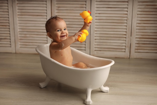 ein 11 Monate altes Baby badet in einer weißen Babywanne mit Gummienten