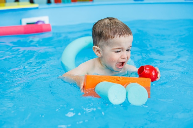 Ein 2-jähriger Junge lernt mit einem Trainer in einem Pool schwimmen. Schwimmunterricht für Kinder. Schwimmschule für Kinder. Pädagogische Schwimmkurse für Kinder
