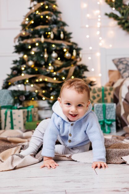 Ein 2-jähriger kleiner Junge sitzt in der Nähe eines Weihnachtsbaums, der mit Spielzeug geschmückt ist. Neujahrsatmosphäre