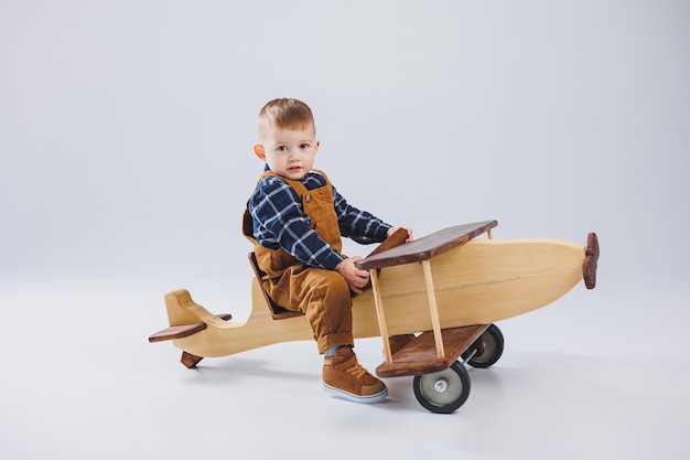 Ein 3-jähriger Junge in einem karierten Hemd sitzt auf einem großen Holzflugzeug Umweltfreundliches Kinderspielzeug aus Holz