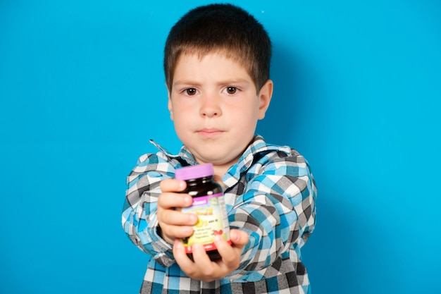 Ein 4-jähriger Junge hält ein Glas Vitamin D oder andere Nahrungsergänzungsmittel auf blauem Hintergrund in der Hand