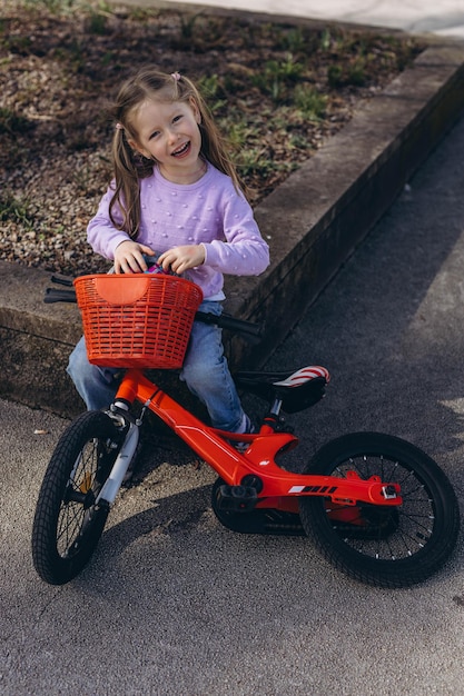 Ein 5-jähriges Mädchen fährt mit dem Fahrrad in einem Park lächelnd und genießt die sonnige grüne Umgebung