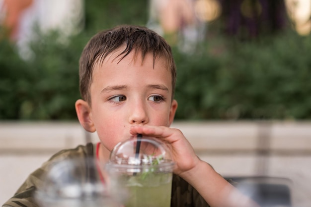 Ein 6-jähriger Junge trinkt Limonade aus einem Strohhalm schaut nicht in den Rahmen seine Haare sind nass