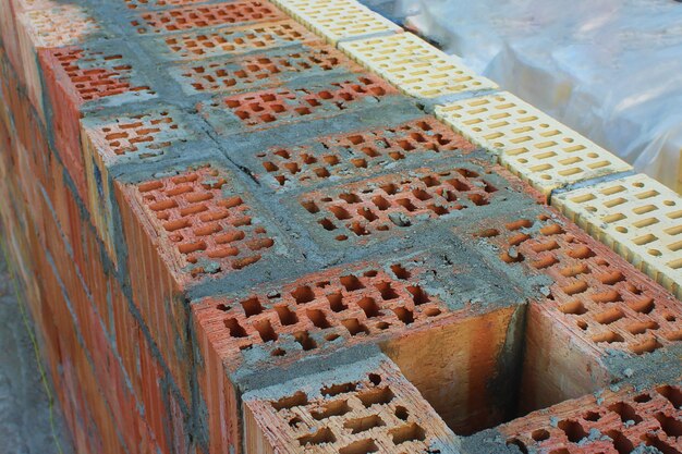 Ein Abluftschacht in einer mit Zement gefüllten Mauer aus rotem Backstein. Verkleidung mit gelben und braunen Ziegeln. Selektiver Fokus. Aufbau Konzept. Unfertiges Haus als Symbol des Bauens.