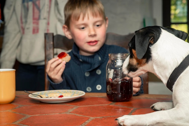 Ein achtjähriger Junge isst mit einem Hund an einem Tisch