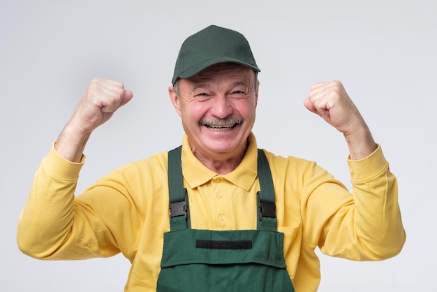 Ein älterer Arbeiter mit grüner Mütze und Kleidung, der aufgeregt die Fäuste hochhält