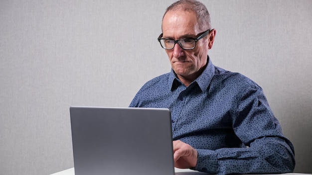 Ein älterer Mann arbeitet am Computer und sitzt am weißen Schreibtisch im Büro